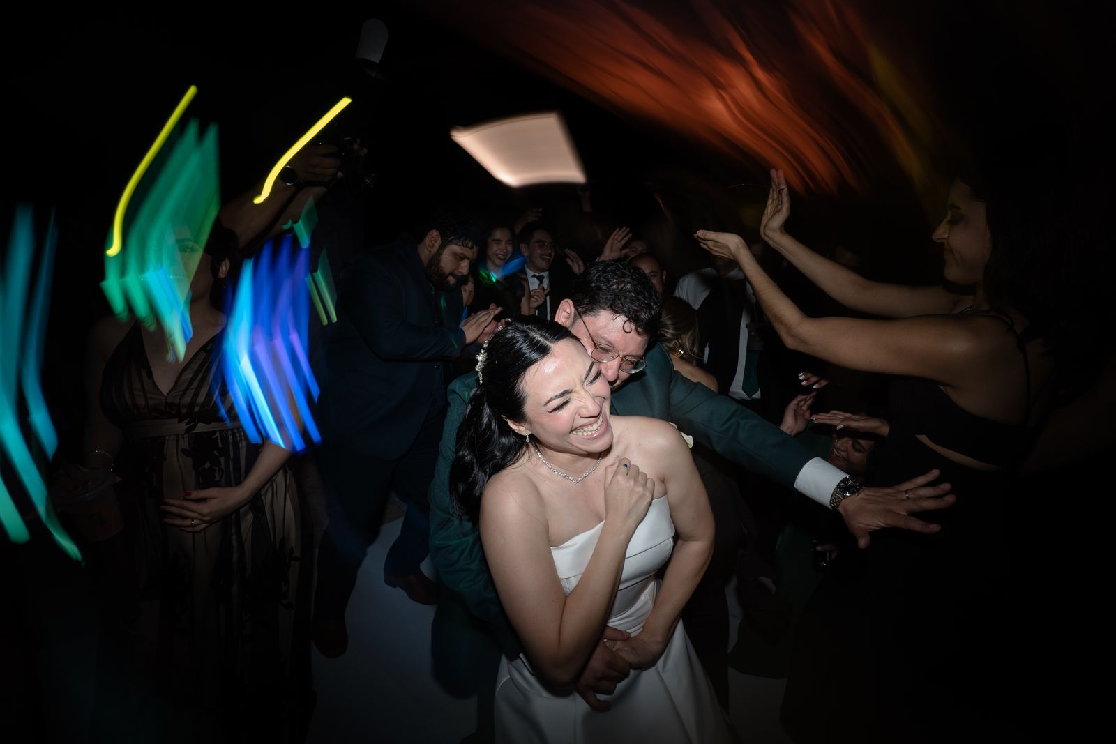 Los novios abrazados en la pista rodeados de invitados, con efecto de movimiento y estelas de luz