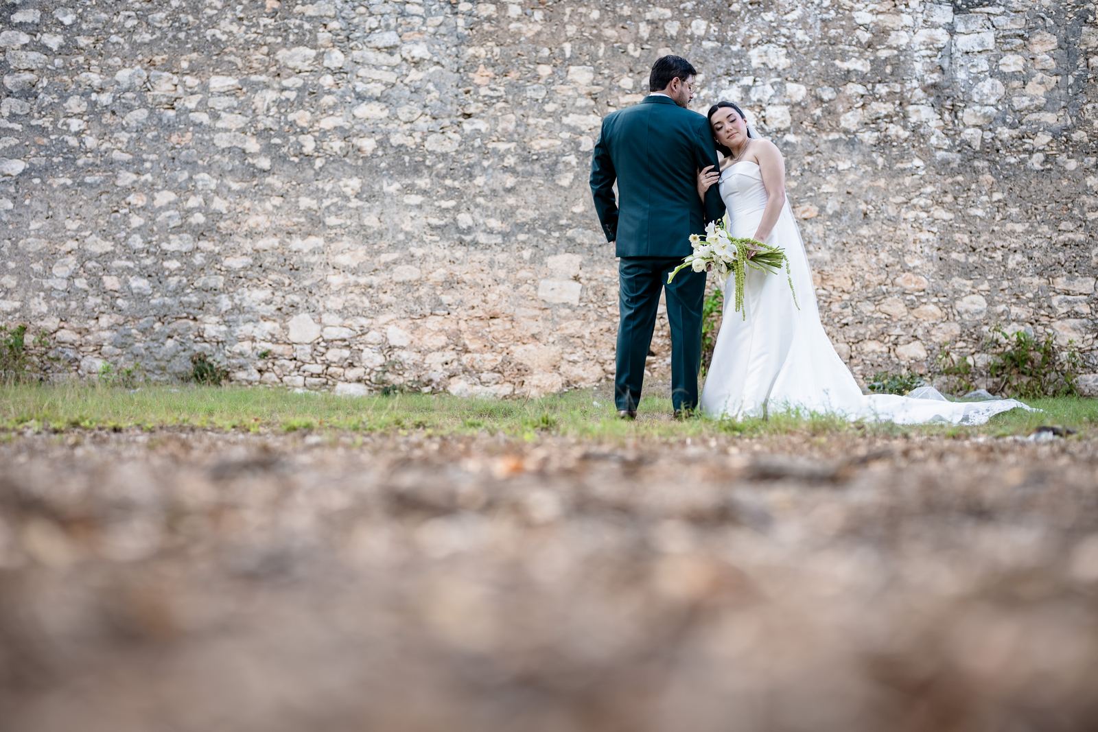 Los novios abrazados junto a un muro de piedra de hacienda