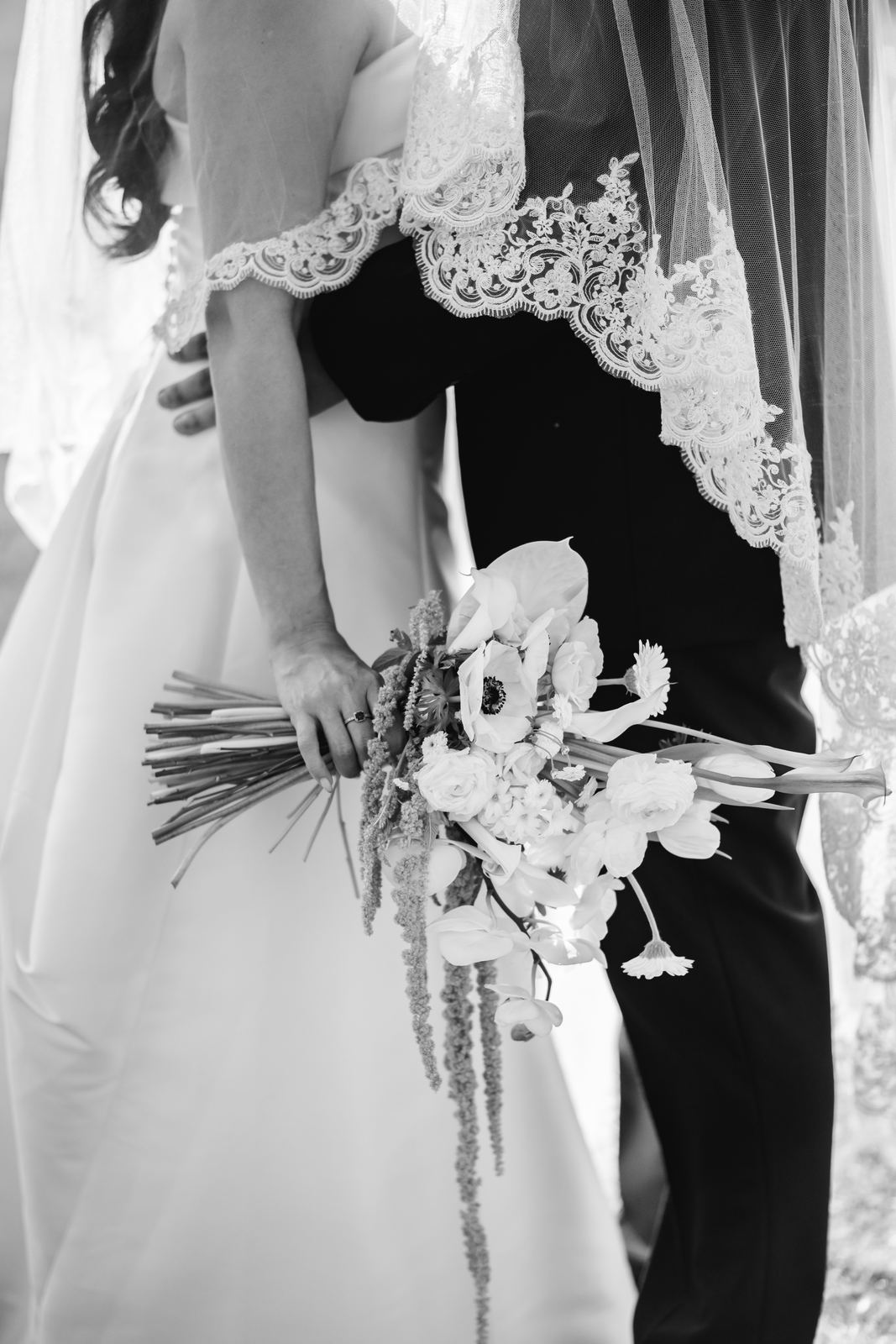 La novia sostiene el ramo a su espalda mientras abraza al novio, en blanco y negro