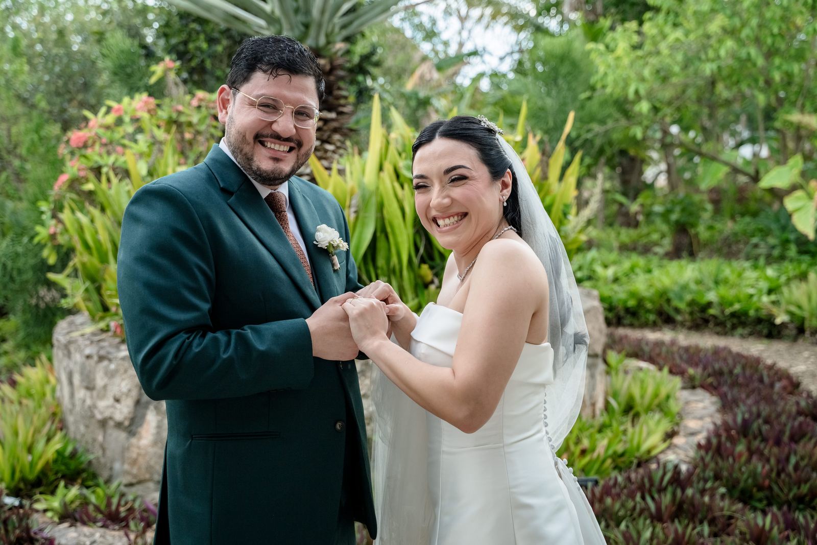 Los novios ríen tomados de las manos en un jardín tropical